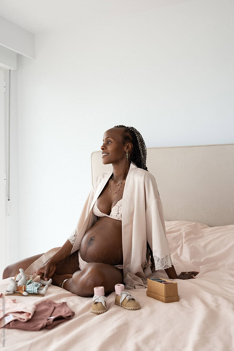 Smiling pregnant woman sitting with baby clothes
