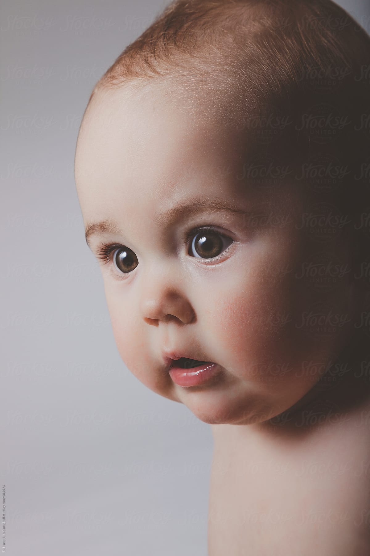 Cute baby girl staring wide-eyed on solid background