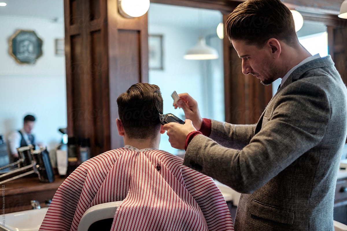 A gentleman barber uses a comb & electric clippers to cut a clients hair.