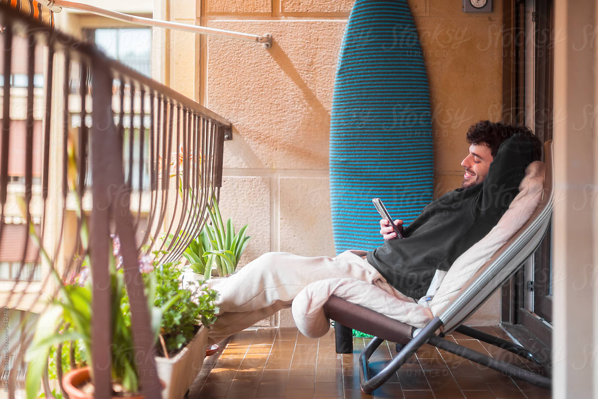 Relaxed man playing with smartphone at home balcony