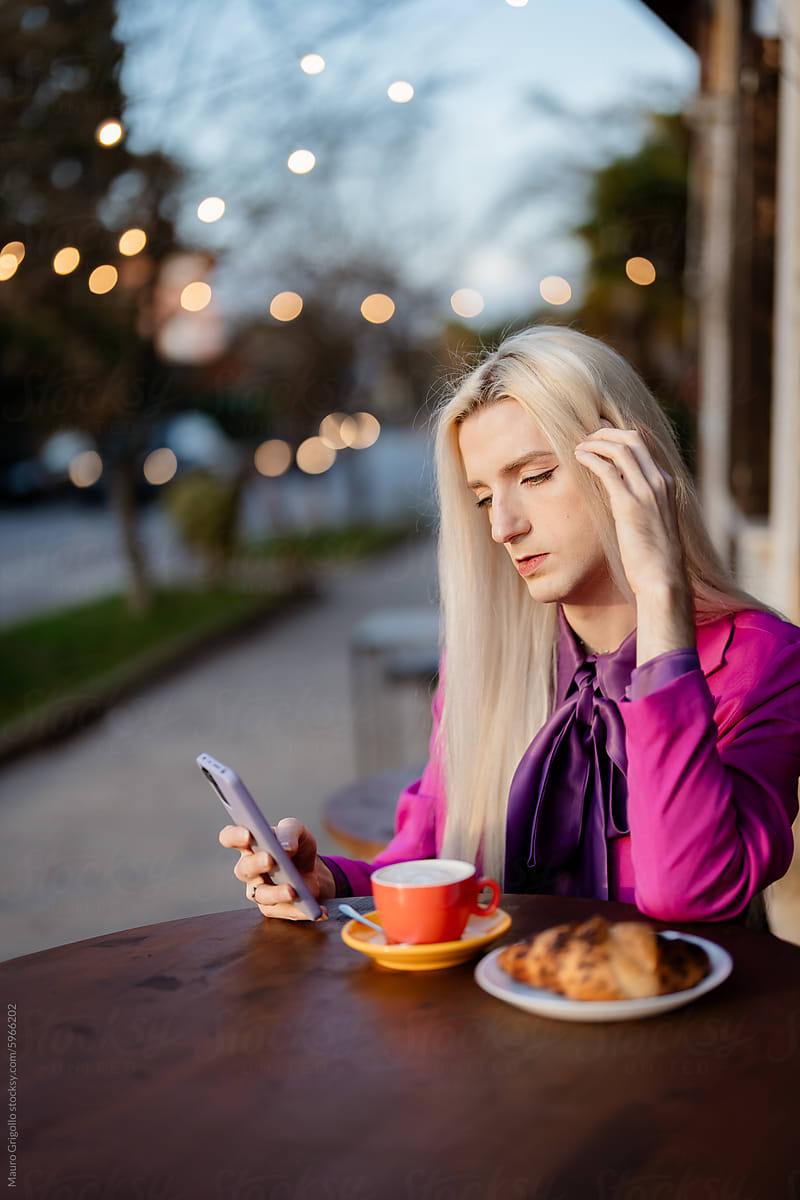 A blond man in pink clothes having breakfast and using a smartphone