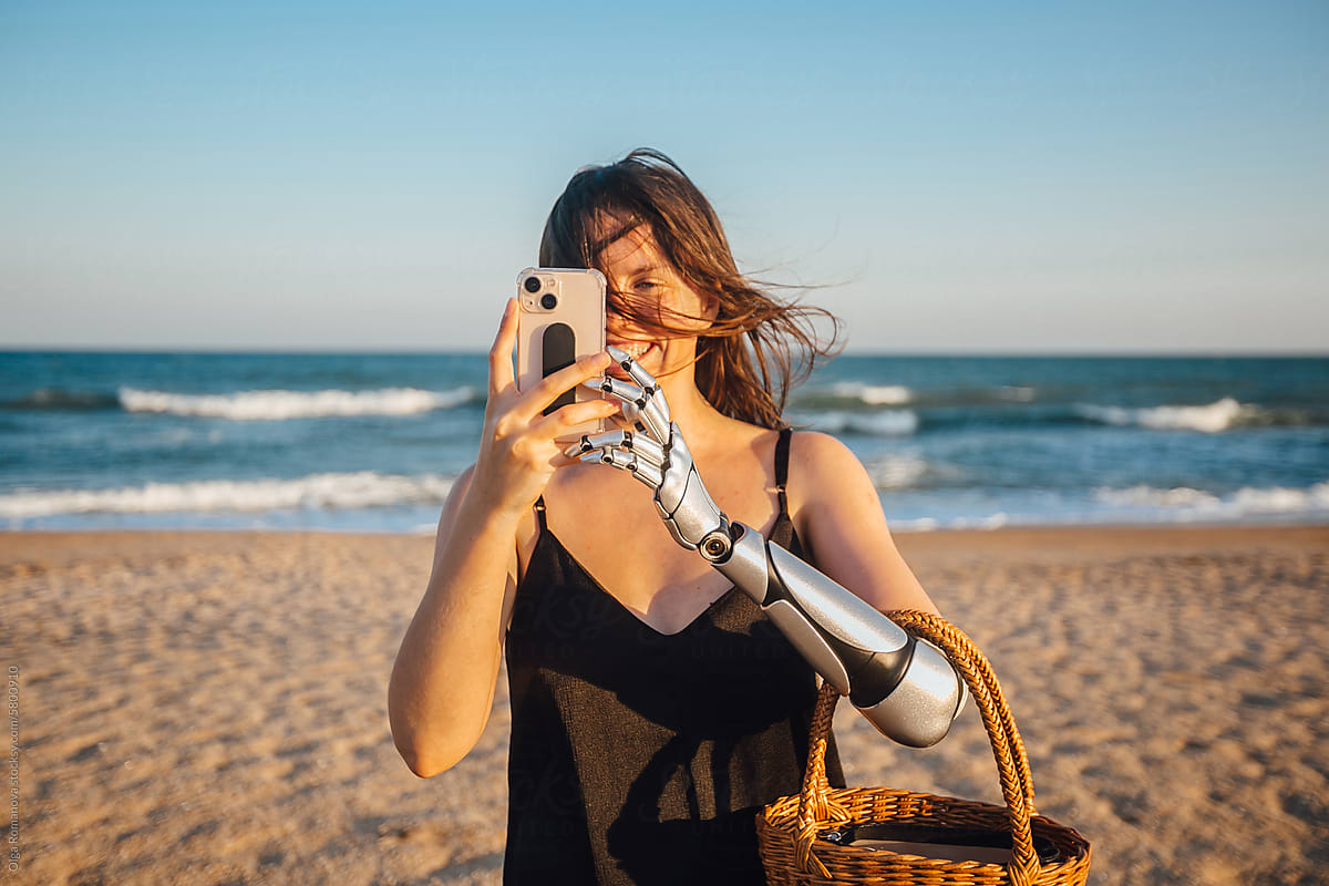 Smiling woman with arm prosthesis and a mobile phone near the sea