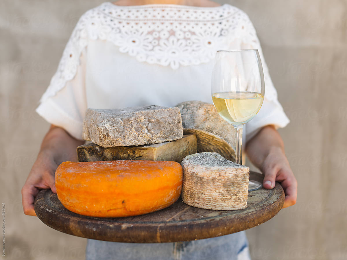 Woman holding a tray with different cheeses and a glass of wine