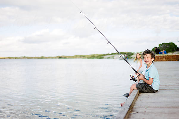 Pre-teenage Girl Sitting On A Dock Beside Her Brother Fishing by