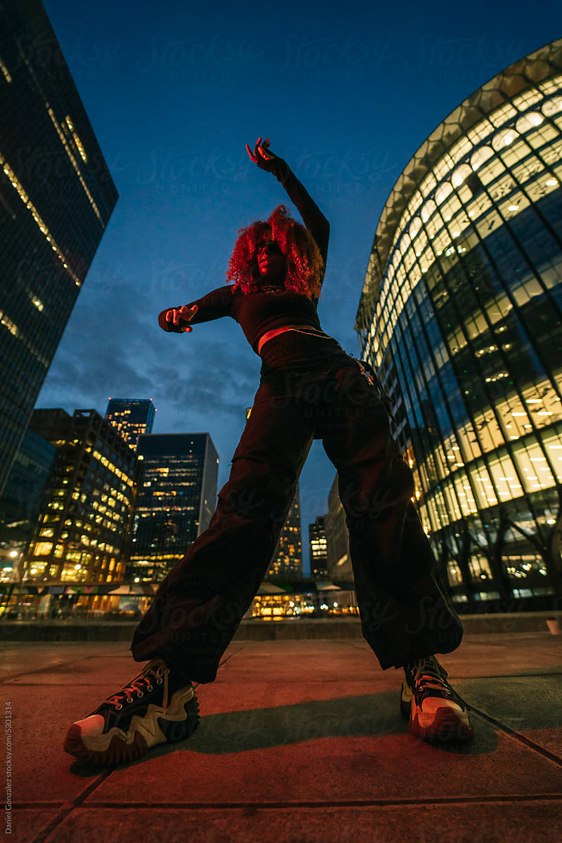 Stylish African American girl dancing on street against skyscrapers