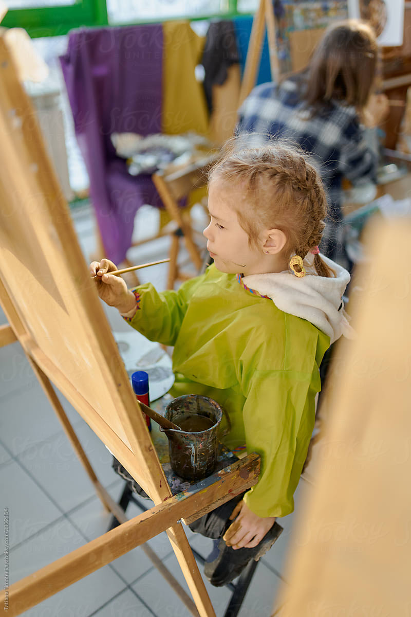 girl in uniform at a drawing class, drawing with paints at an easel