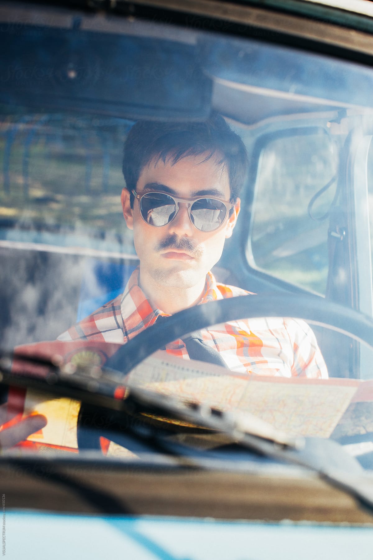 Young Man With Sunglasses Sitting in Vintage Car and Looking at Road Map