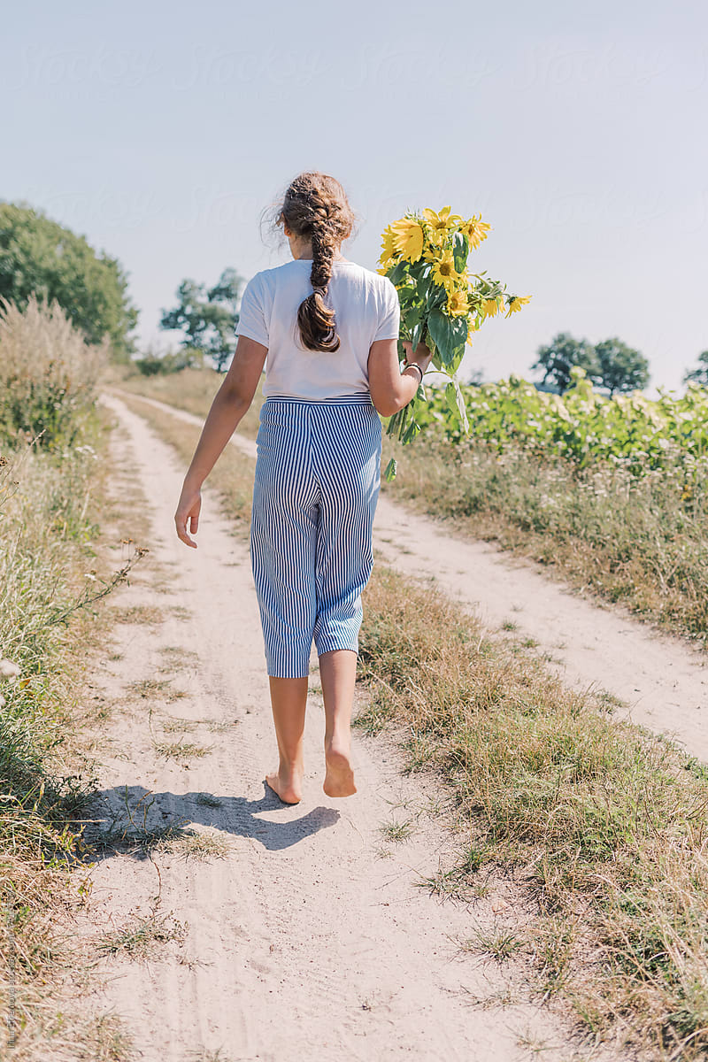 11-Year-Old Girl Walking Along the Road by the Sunflower Field