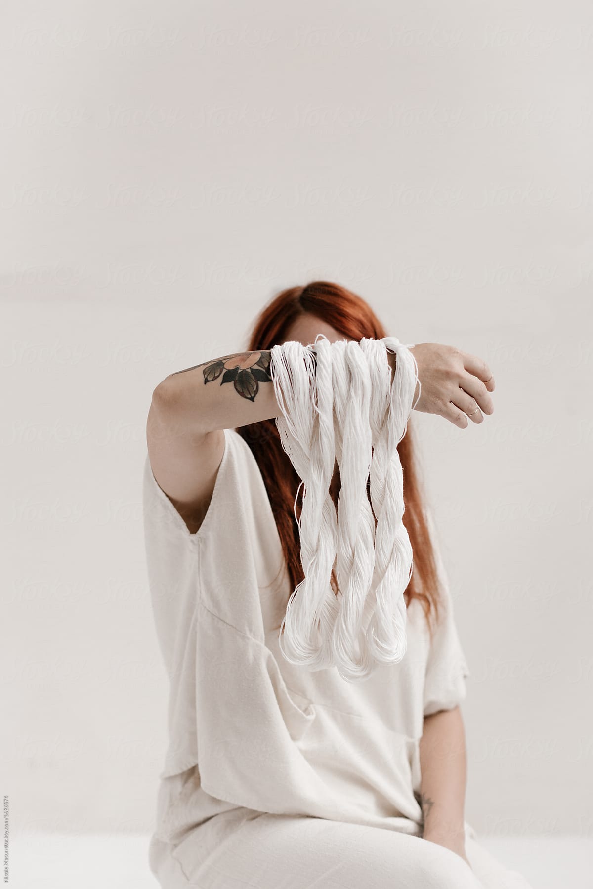 female redhead artist holding three loops of white string in front of face