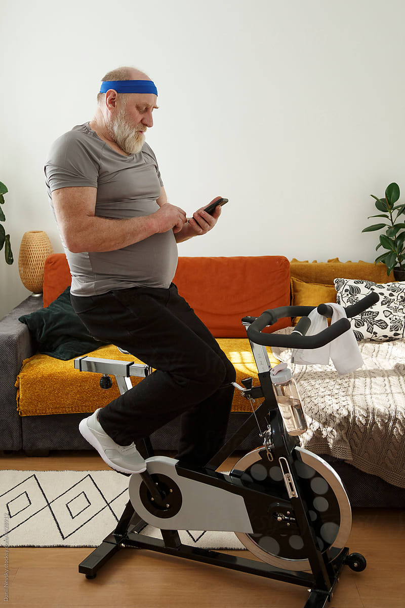 Elderly man using mobile phone on exercise bike