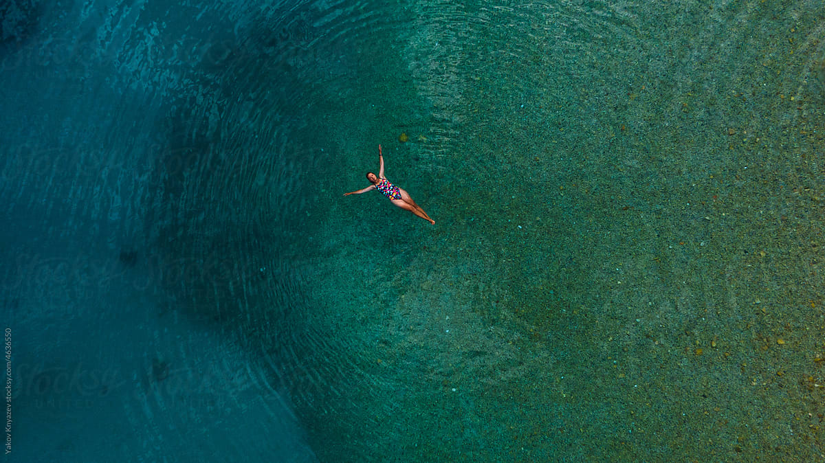 young woman laying on turquoise water, drone overhead