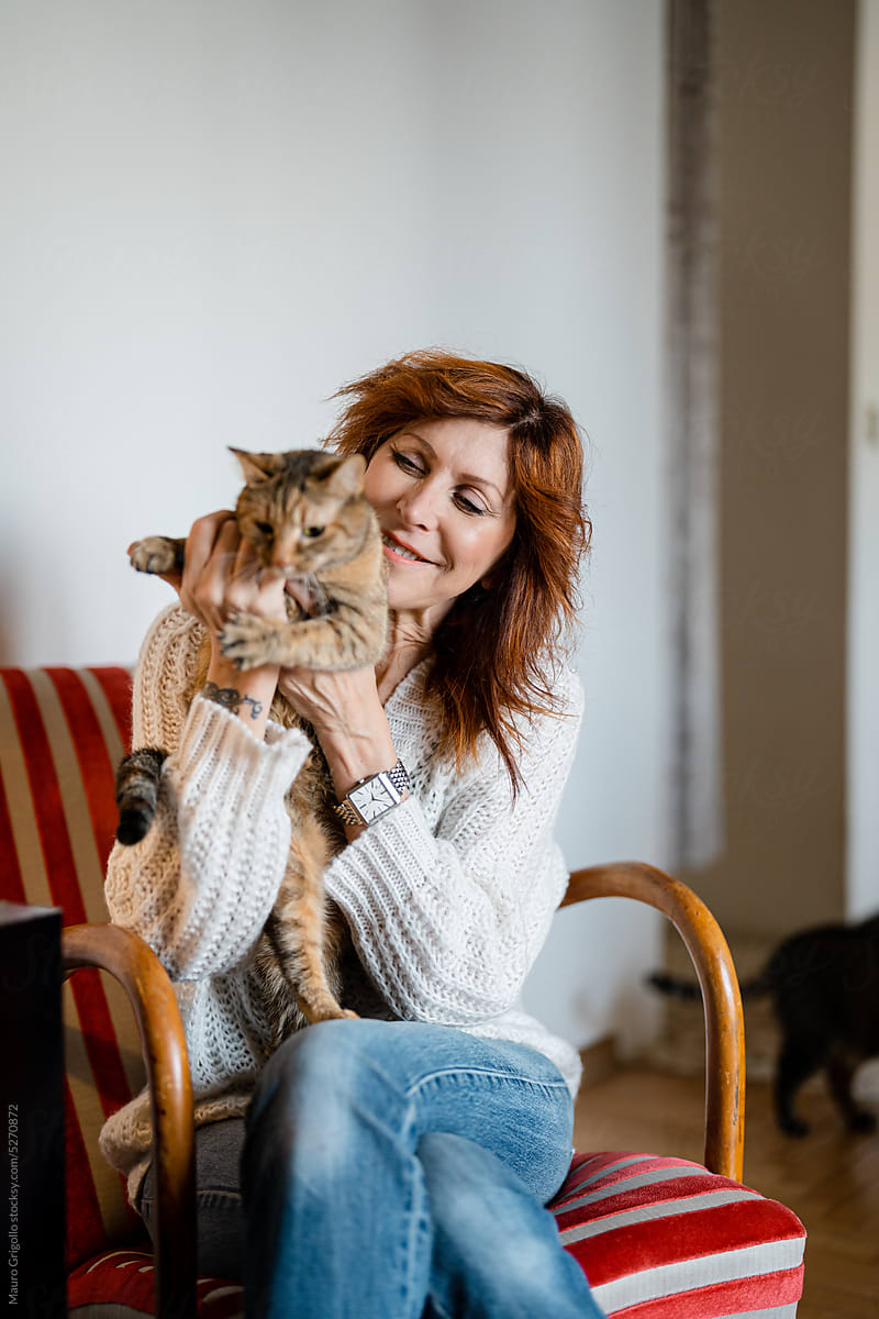 A woman strokes her cat while sitting on an armchair