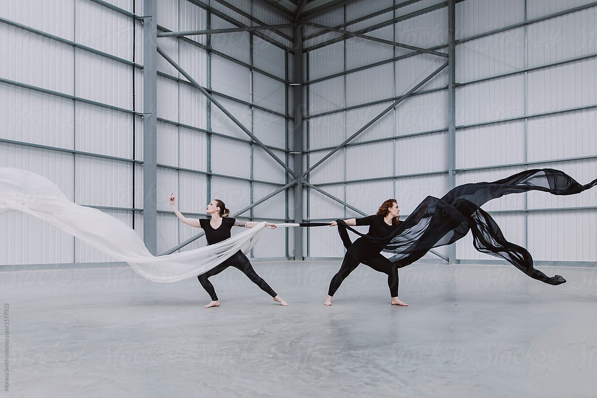 Two female dancers holding onto black and white silk, leaning and balancing away from each other