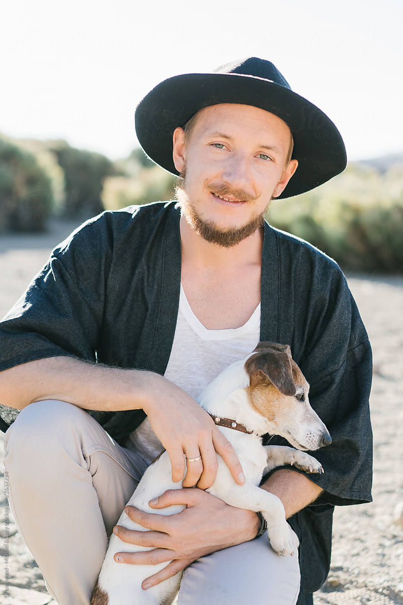 Adult man sitting on sand and hugging dog