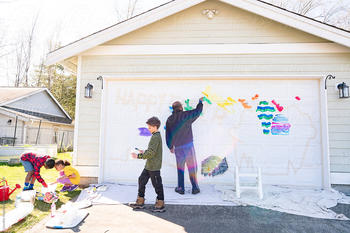 Black dad and three children paint mural on house garage door