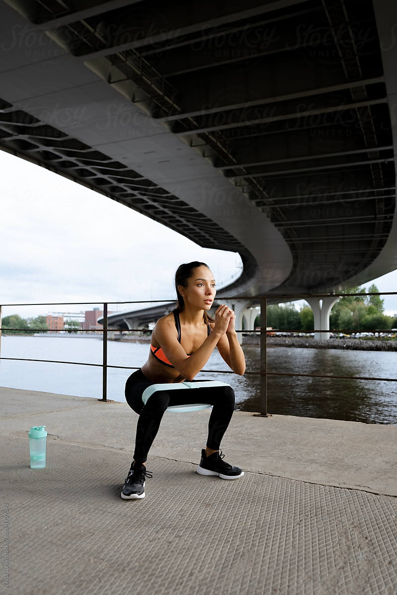 Sporty woman doing squats with fitness gum expander outdoors