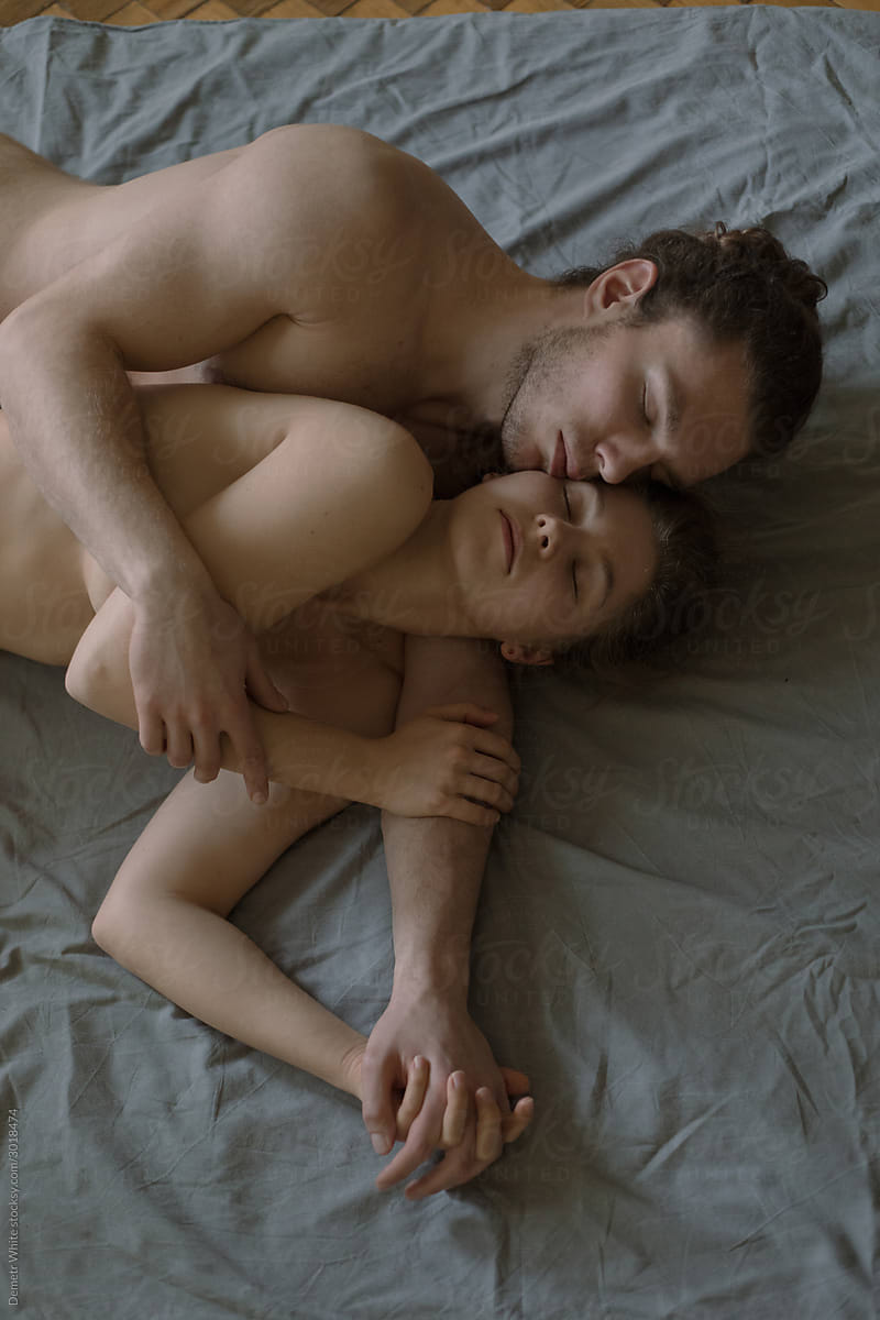 guy and girl lie on a blanket of neutral color naked in an embrace