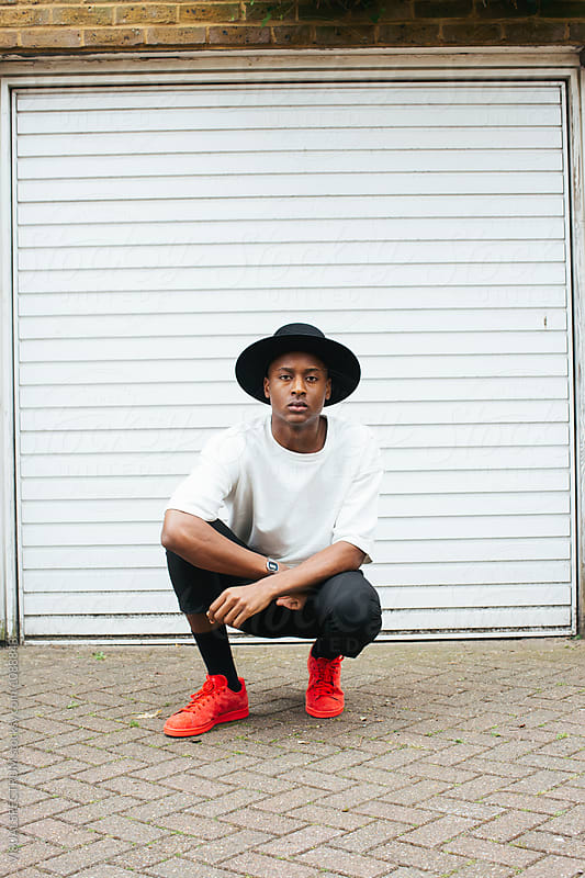 Street Style - Outdoor Portrait of Cool Young Black Man Crouching in Front of White Garage Door