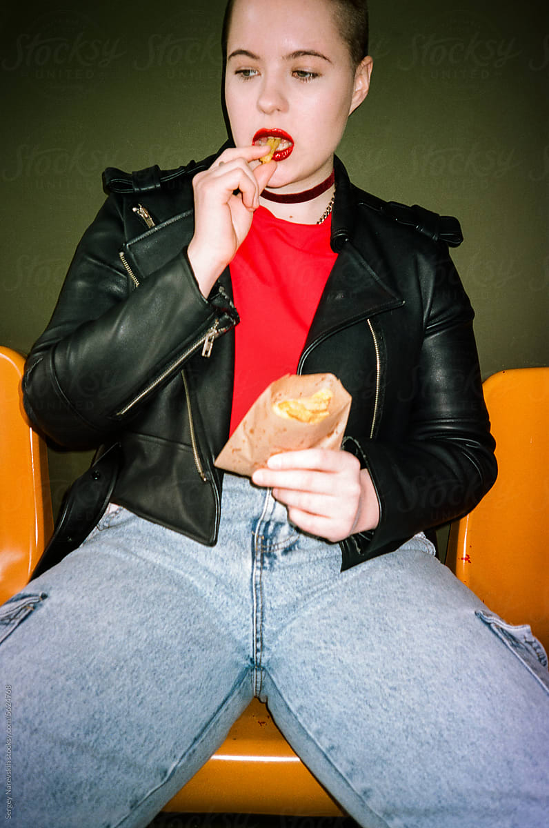 Stylish woman in leather jacket eating fries