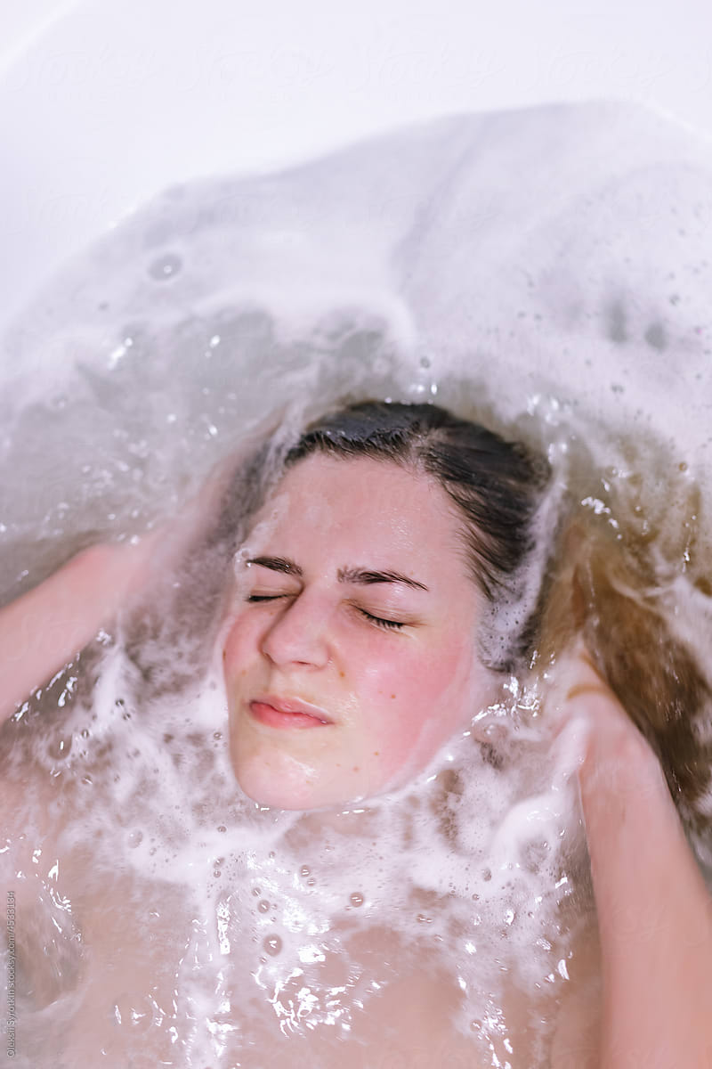 Atrtractive girl squinting eyes while immersing hair in water