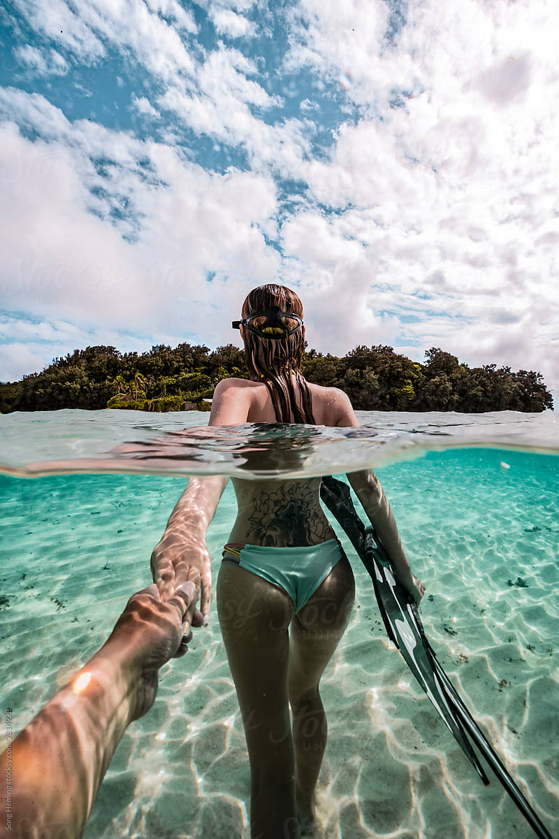 Photographer stretch out hand in hand with  female standing half underwater with fins