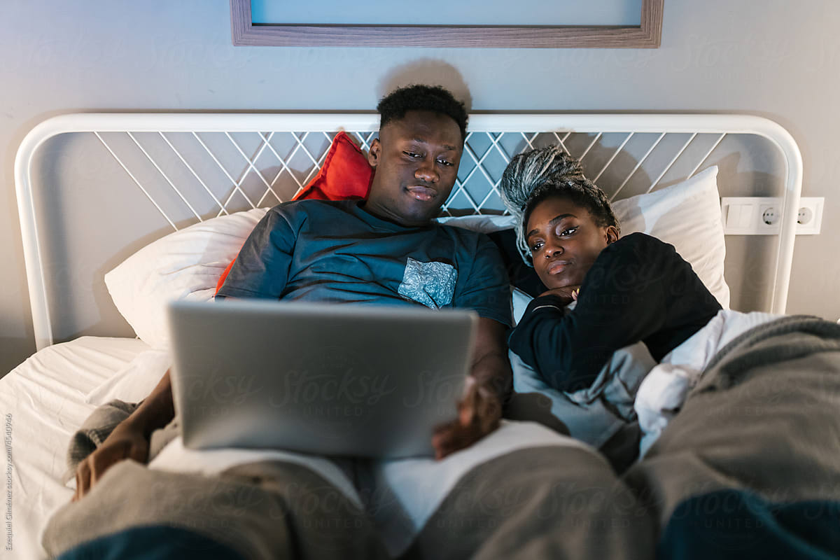 Romantic couple looking at photos on their computer in bed.