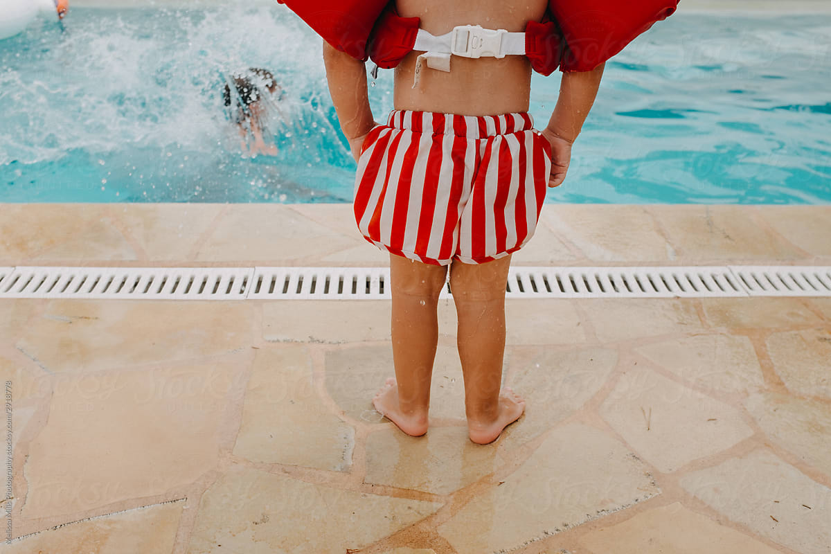 a little boy standing in front of a pool, ready to jump