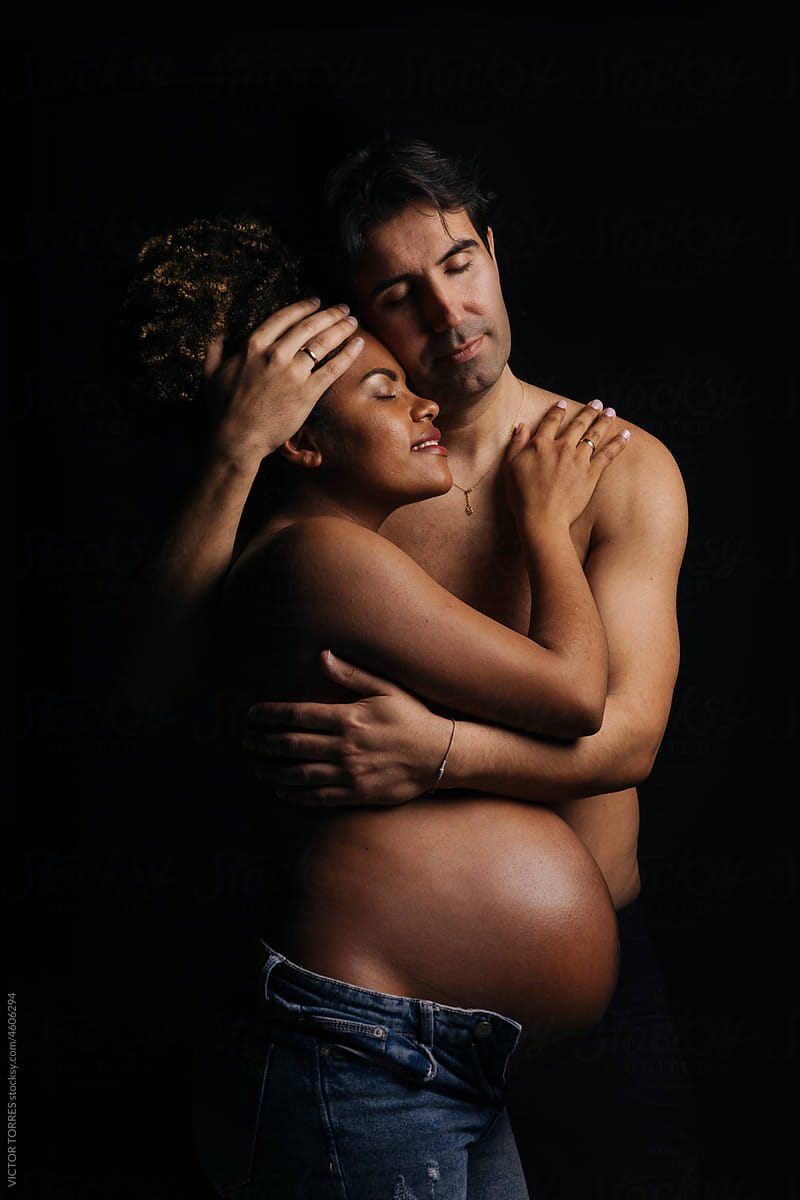 Sensual naked pregnant couple hugging in dark room