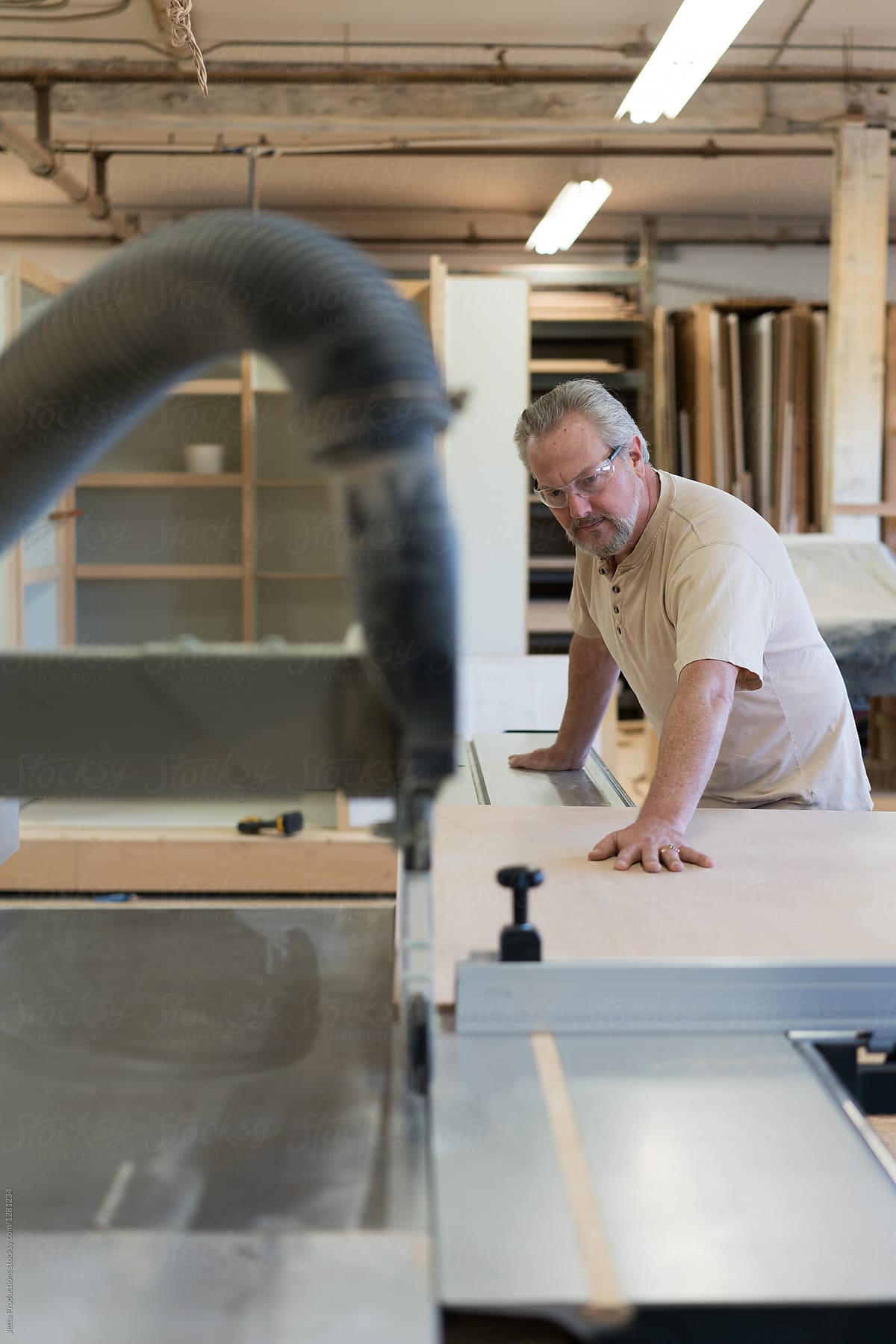 Carpenter feeds a sheet of plywood into a commercial router in a
