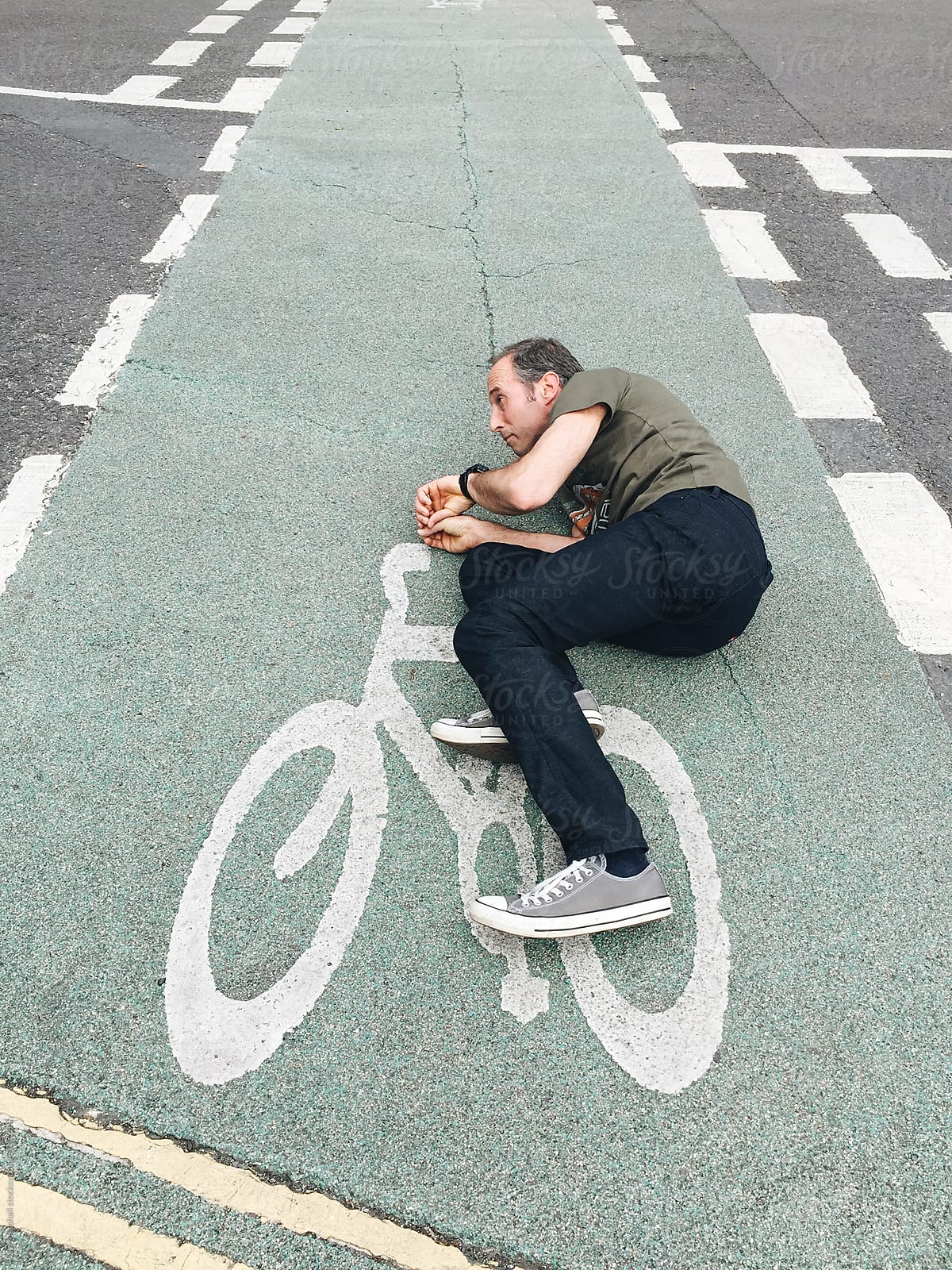 Man lying on tarmac pretending to ride a bicycle that is painted on the road