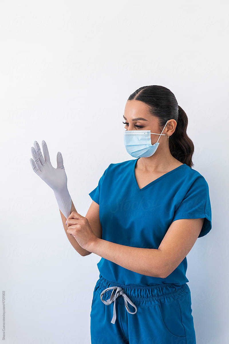A doctor putting on gloves in front of a white wall
