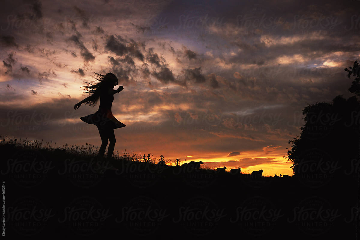 A silhouetted girl dances across a field at sunset