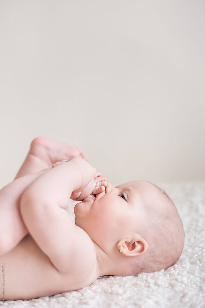 Beatiful naked chubby baby chewing her toes.