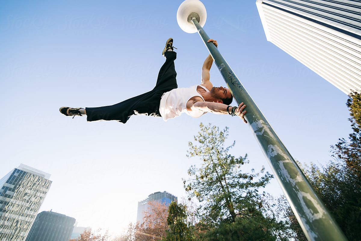 Man holding on to lamp post doing the human flag trick during a parkour session