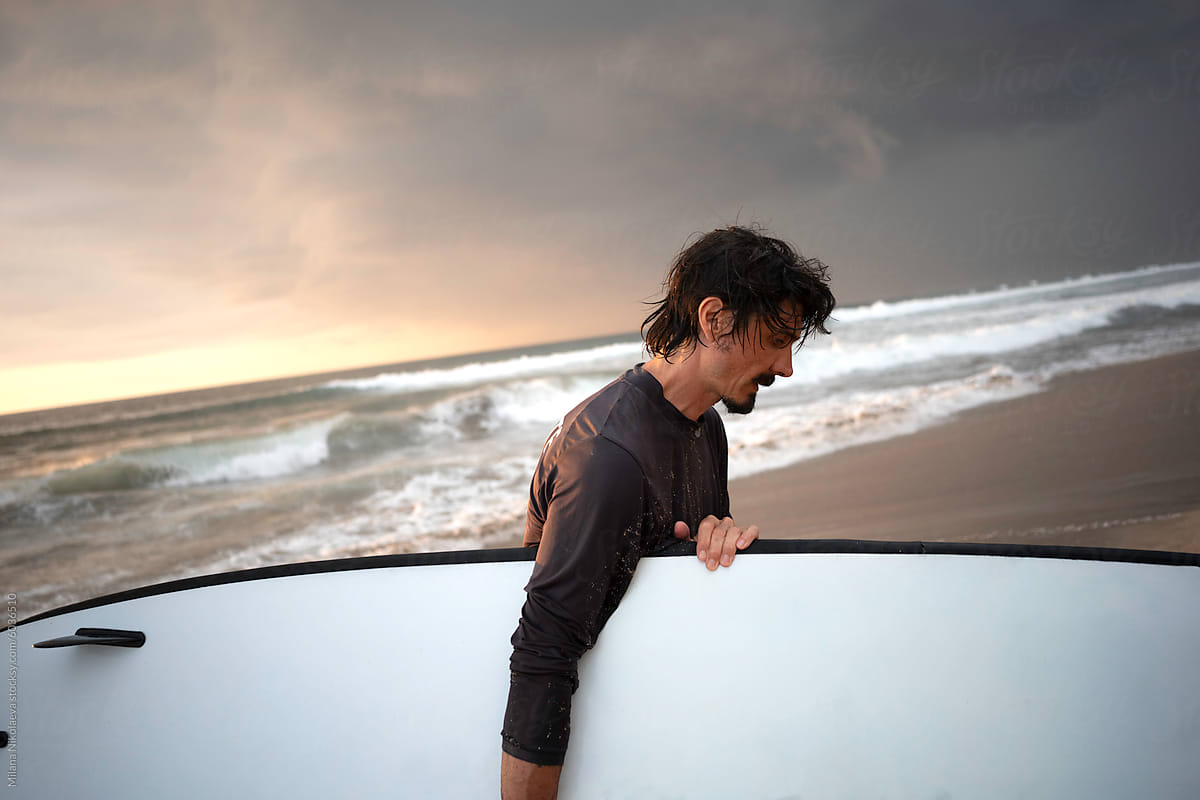 Male Surfer Walking Towards the Waves at a Sandy Beach During Sunset