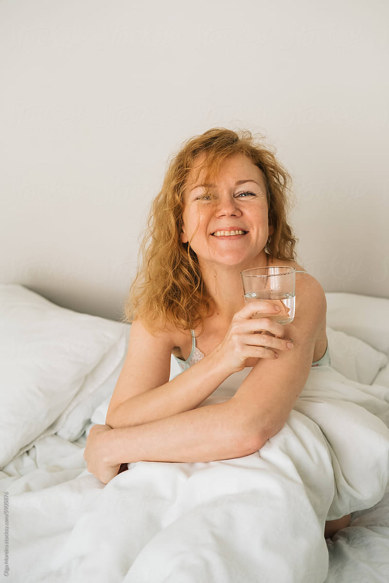 Red-haired woman with glass of water in bed