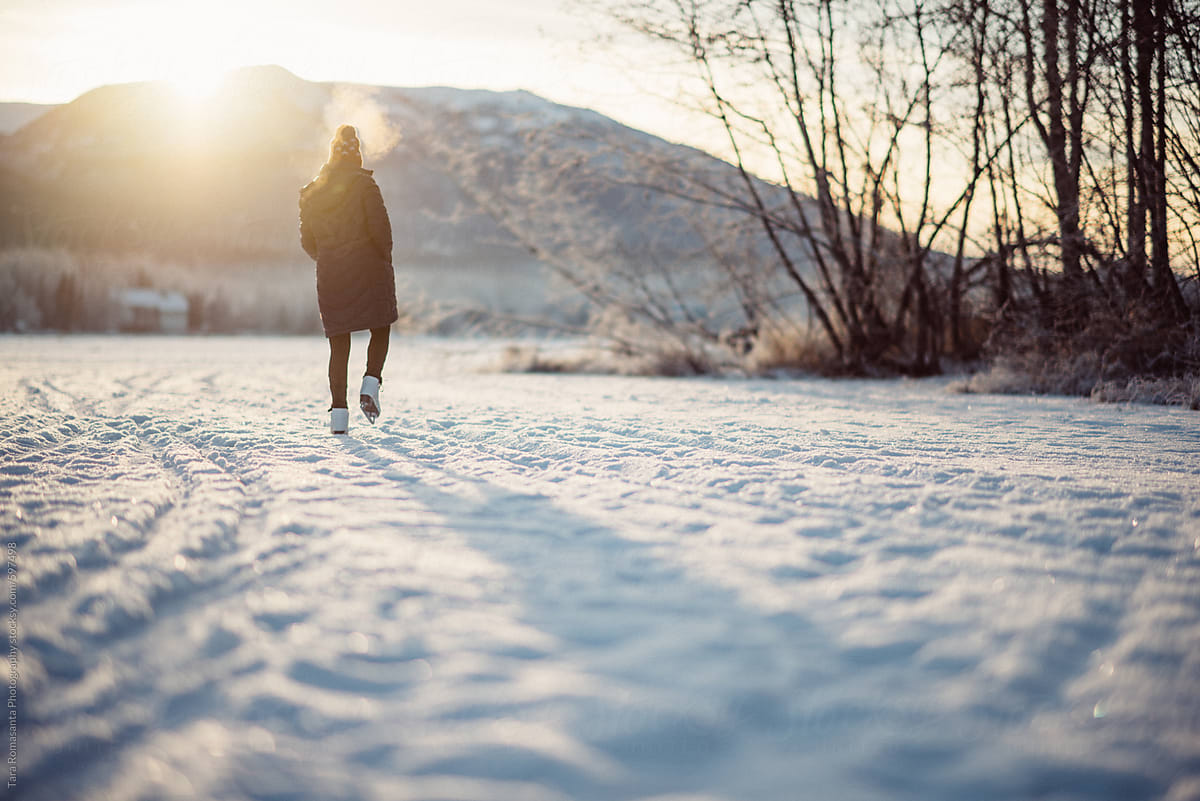 Young woman in ice skates walks carefully over a rough patch of snow covered ice