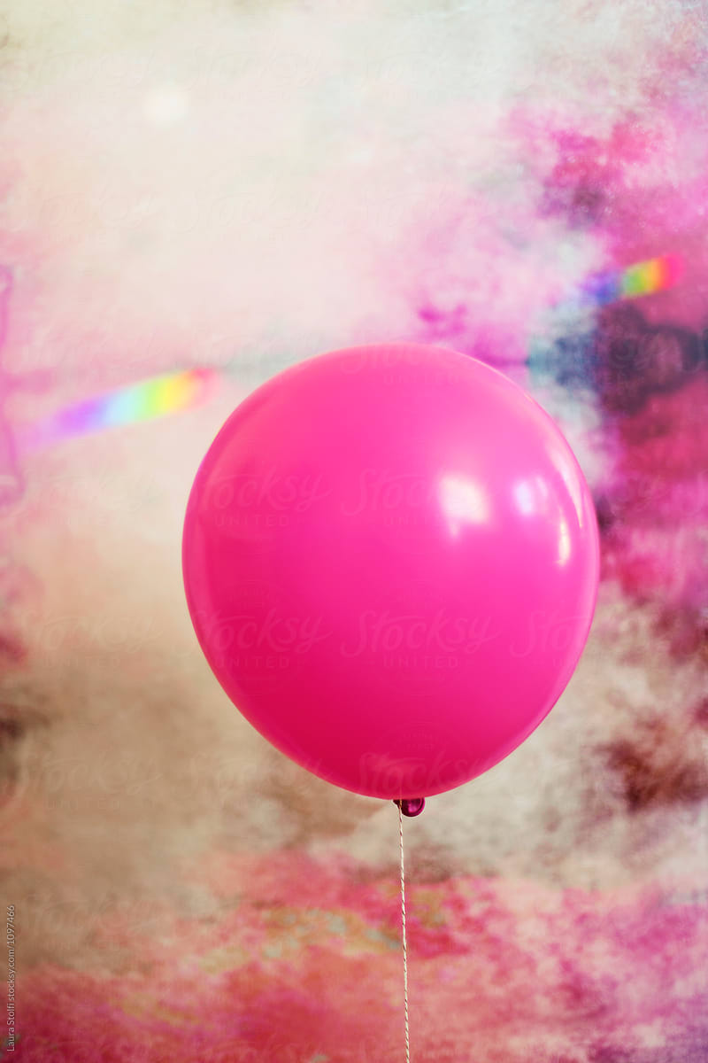 Fluo pink balloon against pink painted wall and rainbow