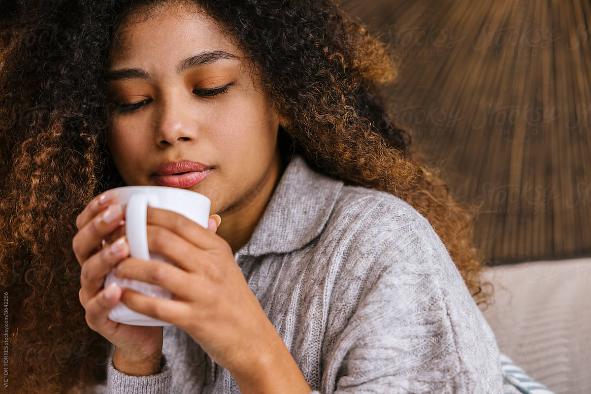 Young latin woman with cup of coffee resting on sofa