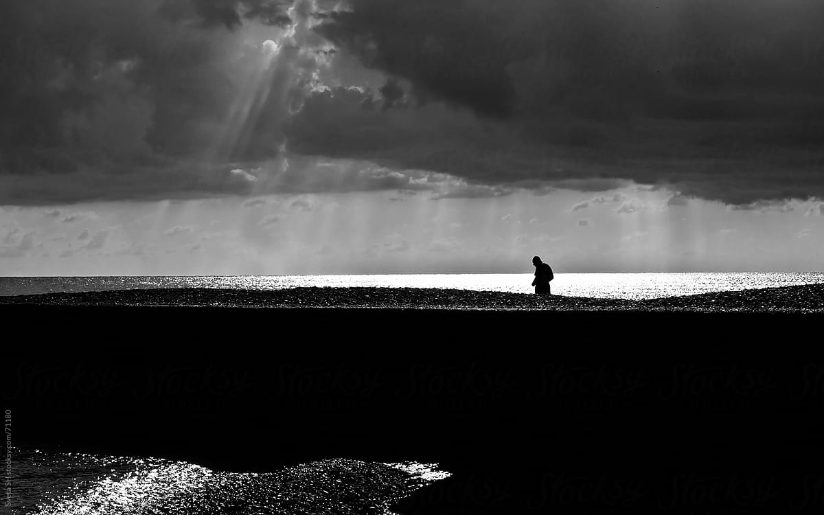 Silhouette of a man walking to the sea on a background of water and sunlight