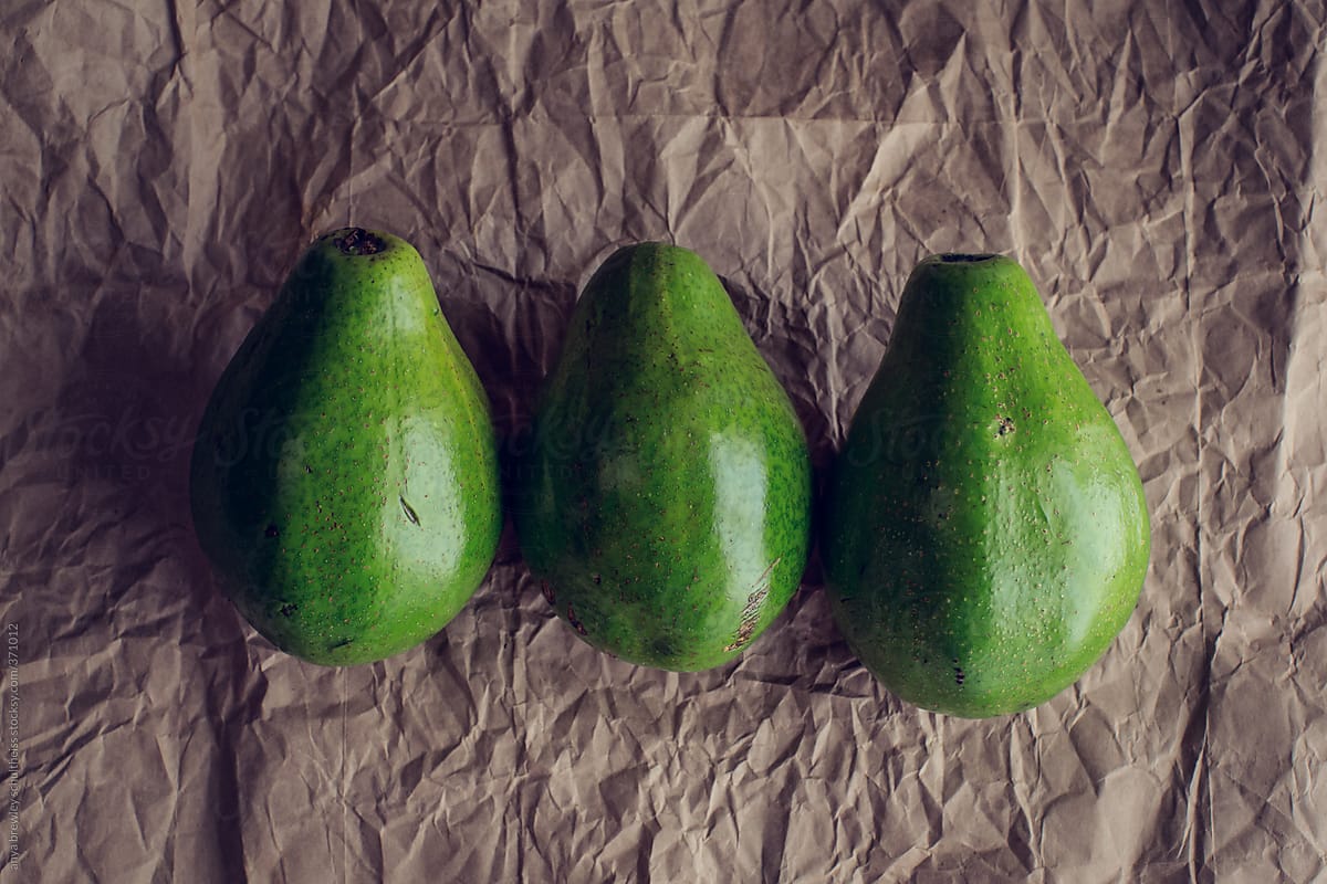 Three green avocados on a brown paper background