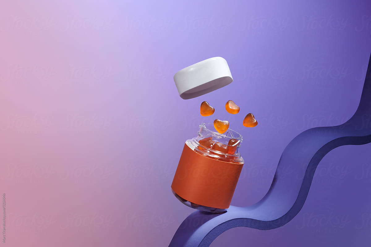 Multivitamin Gummy candies fly out of the jar on orange backgrou