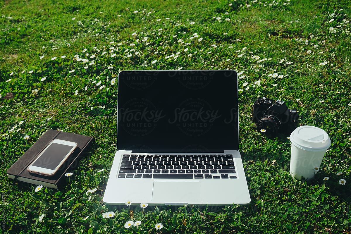 Laptop, phone, notebook, coffee, and camera in a meadow