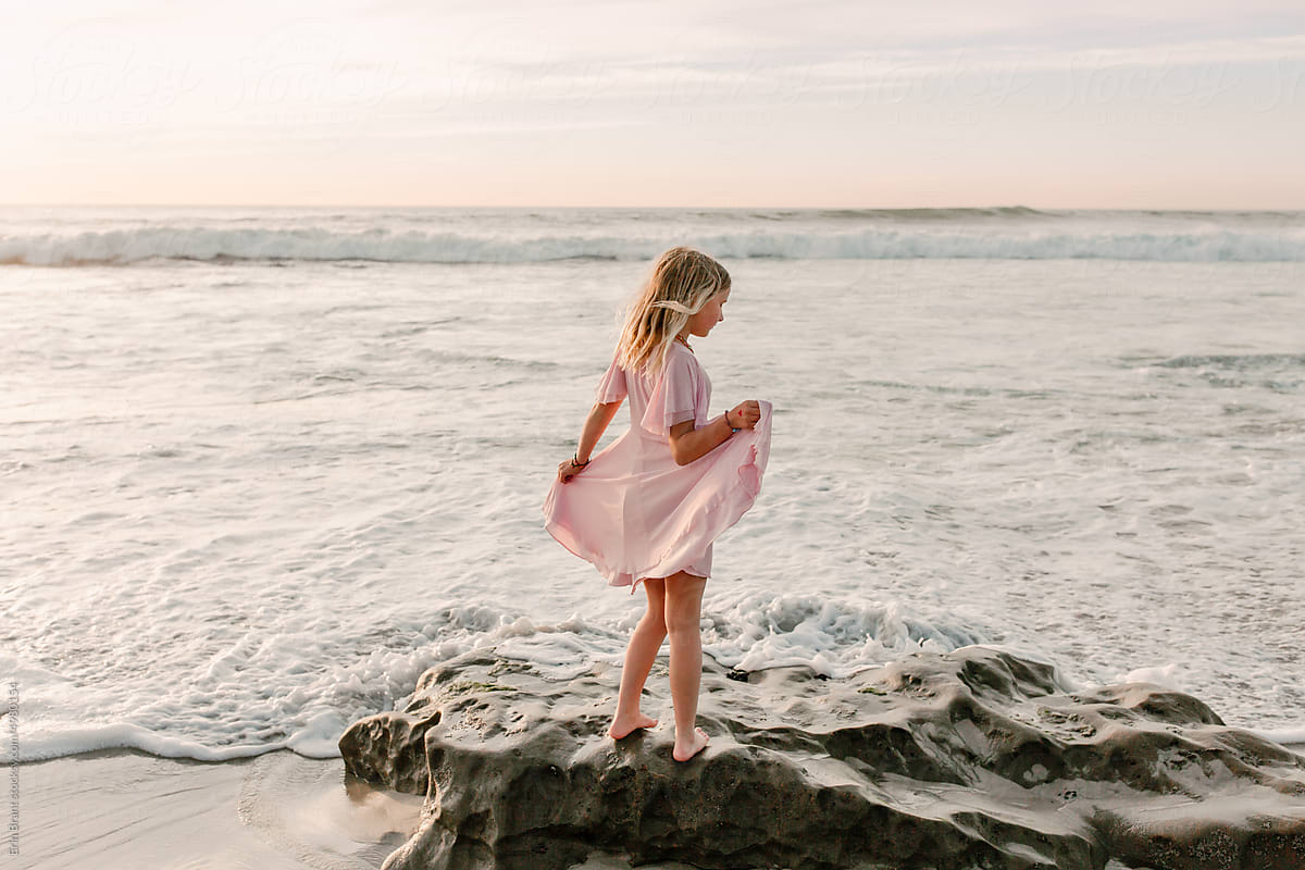 Happy tween girl in pink dress dancing on beach