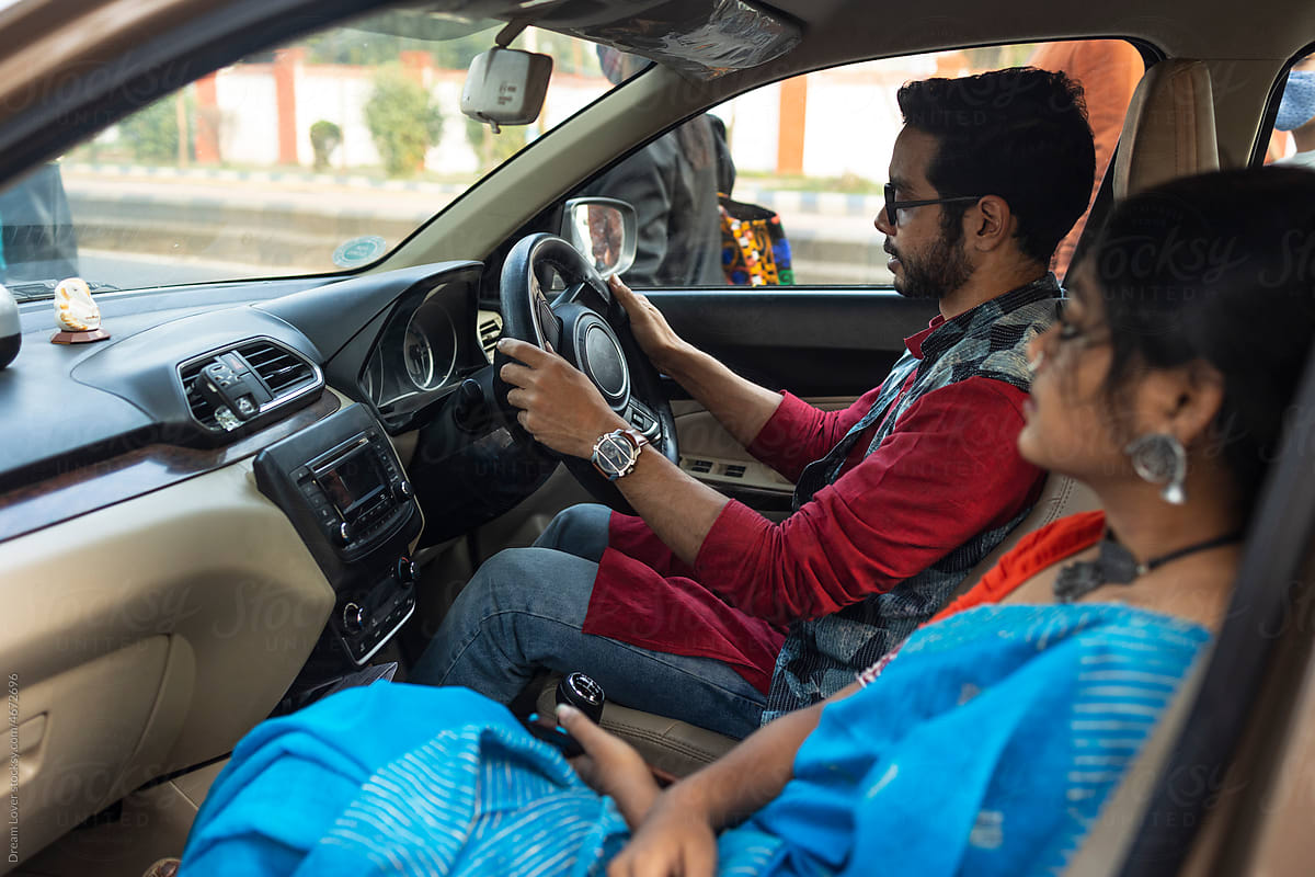 Indian young couple sitting inside a car and browsing smartphone