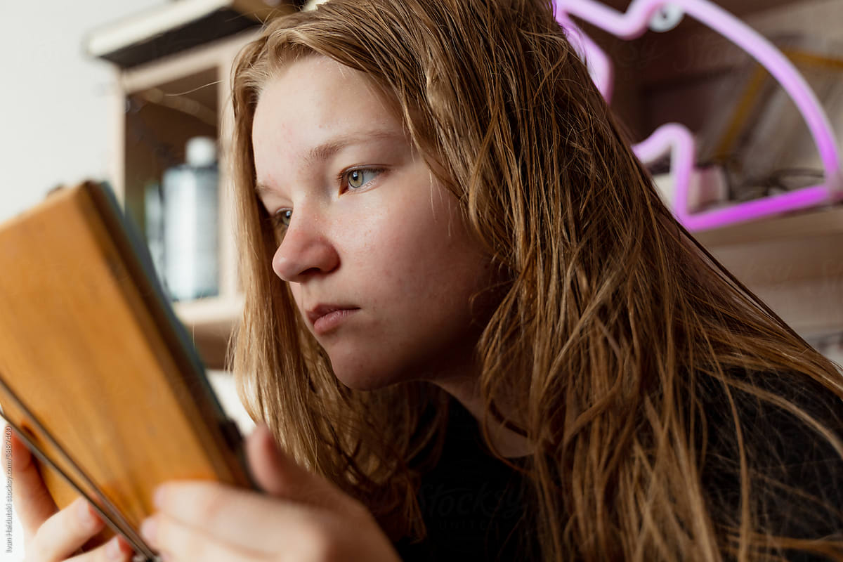 Teen girl sadly examines acne in mirror, facial concerns