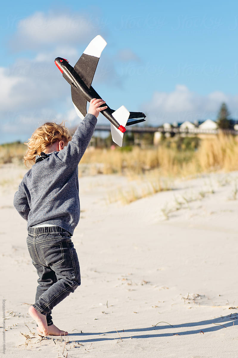 Small boy having fun with a model plane at the beach on a windy day