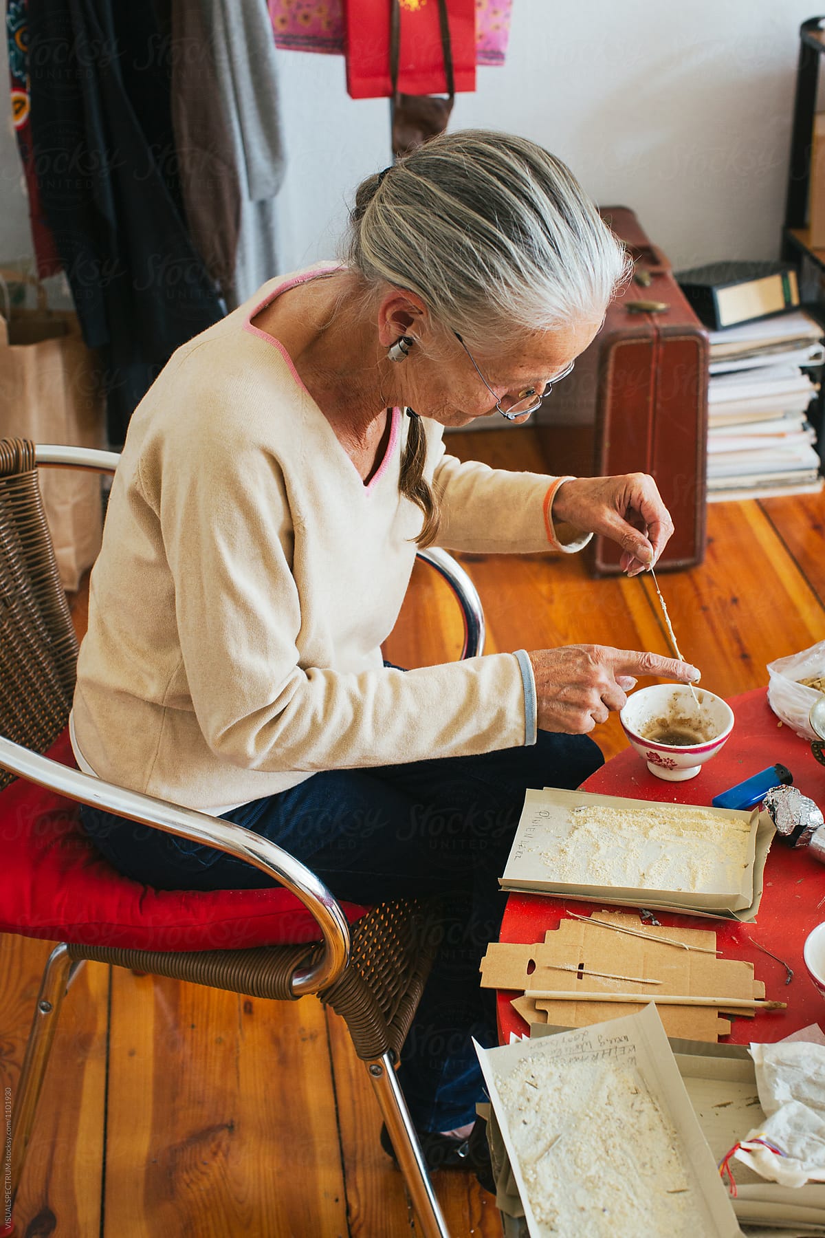 Indoor Portrait of Elderly Female Herbalist with Grey Hair Making Natural Incense Stick