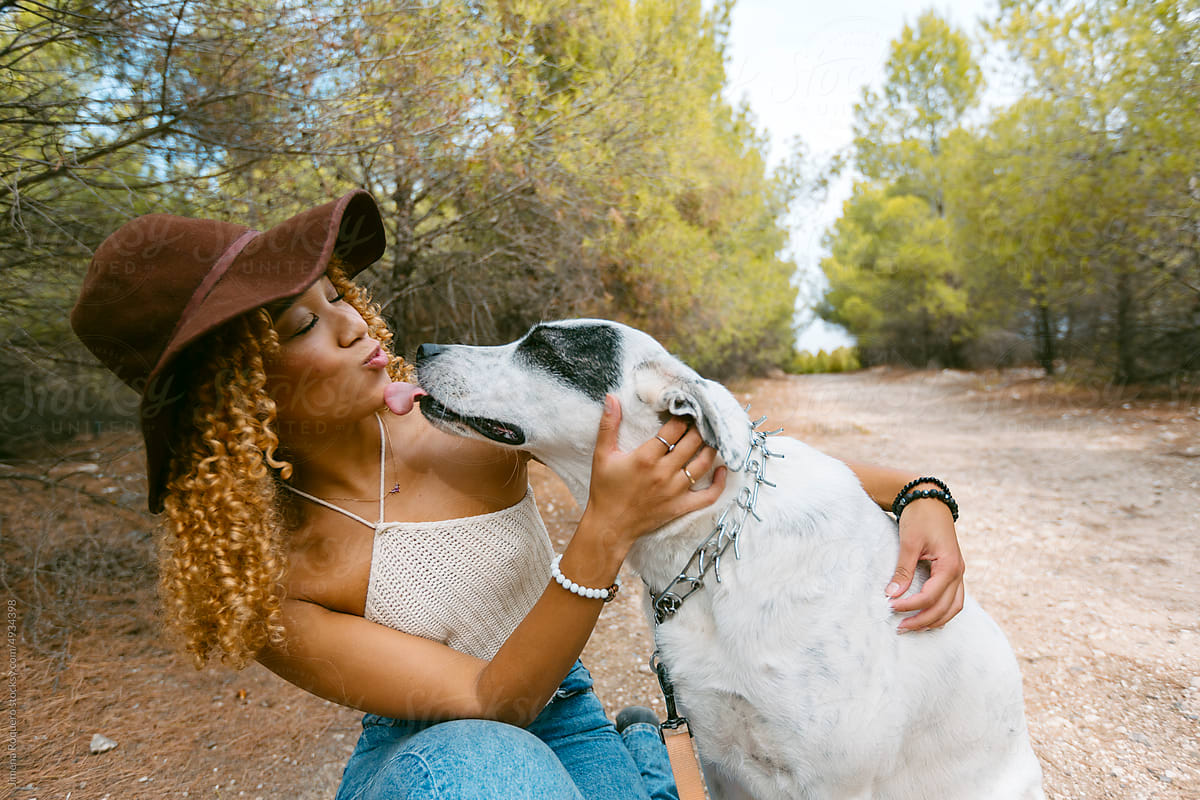 Girl with hat petting her dog outdoor in sunlight laughing