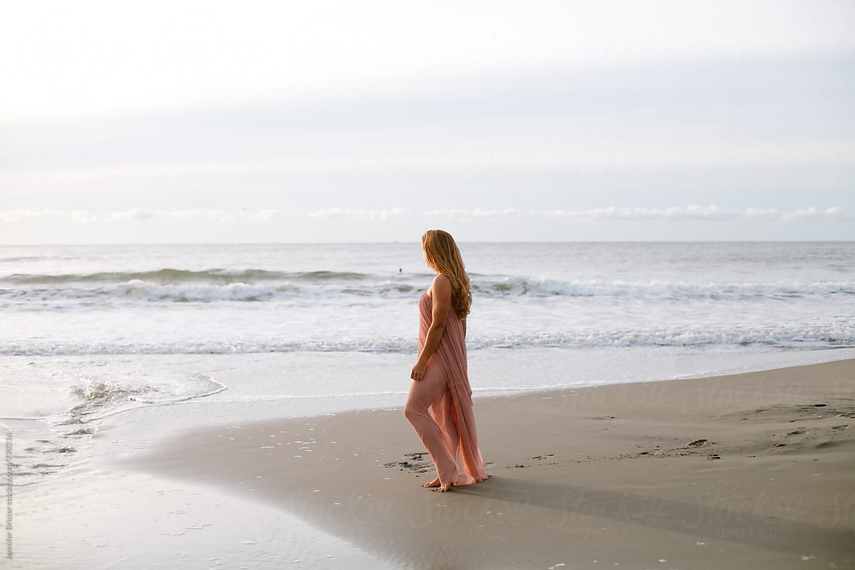 A woman stands on beach facing ocean